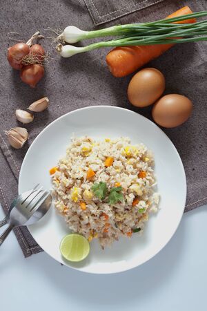 A dish of fried rice, carrot and egg on brown fabric, spoon, folk and ingredients for backgroundの写真素材