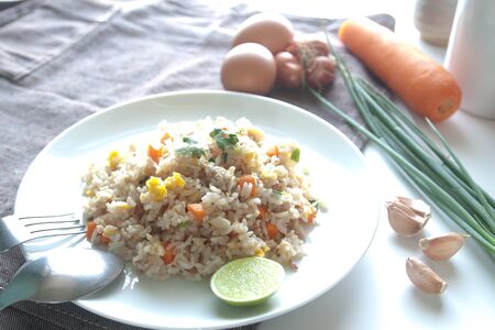A dish of fried rice, carrot and egg on brown fabric, spoon, folk and ingredients for backgroundの写真素材