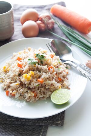A dish of fried rice, carrot and egg on brown fabric, spoon, folk and ingredients for backgroundの写真素材