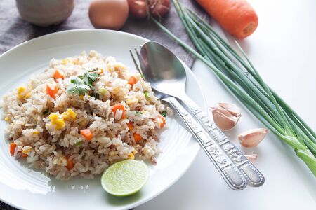 A dish of fried rice, carrot and egg on brown fabric, spoon, folk and ingredients for backgroundの写真素材