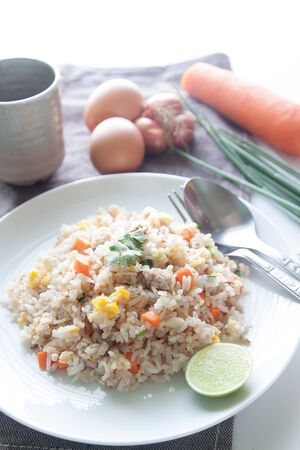 A dish of fried rice, carrot and egg on brown fabric, spoon, folk and ingredients for backgroundの写真素材