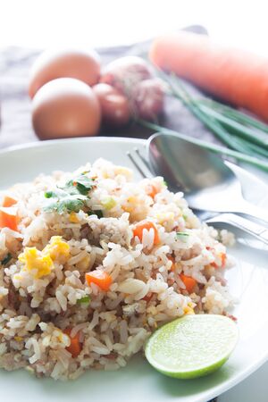 A dish of fried rice, carrot and egg on brown fabric, spoon, folk and ingredients for backgroundの写真素材