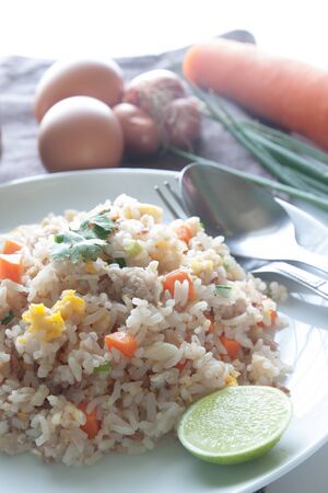 A dish of fried rice, carrot and egg on brown fabric, spoon, folk and ingredients for backgroundの写真素材