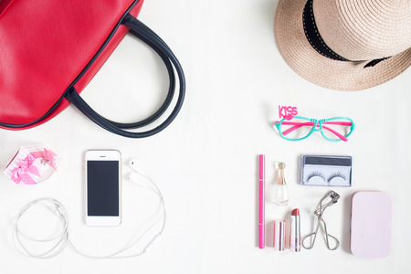 Overhead view of essential beauty items, Top view of smartphone, red hand bag, fashion eyeglasses and cosmeticの写真素材