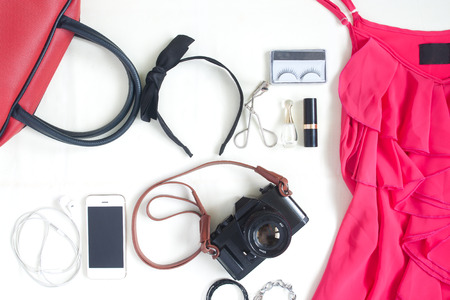 Flat lay of fashion items with film camera, smartphone, red hand bag and beauty items on white backgroundの写真素材