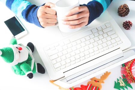 Hands holding cup of coffee and using laptop, smartphone with Christmas decoration, Shopping onlineの写真素材