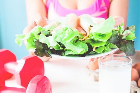 Female fitness holding salad dish with milk, eggs and dumbbells on table, Healthy lifestyle conceptの写真素材