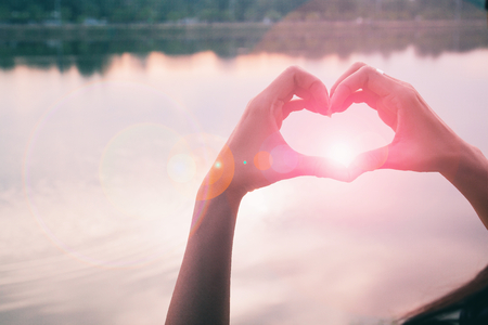 Hand in shape of love heart with sunset reflaction backgroundの写真素材