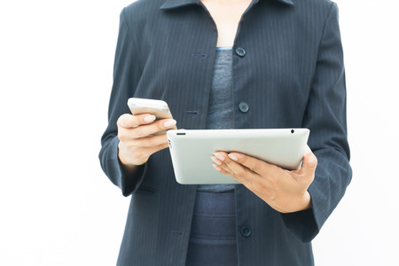 Business woman in dark suit using her tablet and mobile phone on white background with copy spaceの写真素材