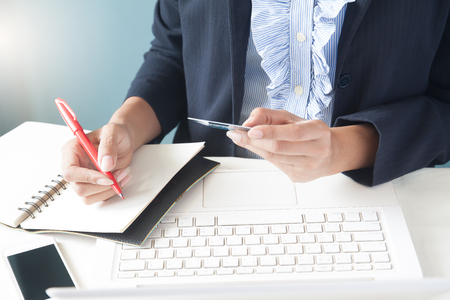 Business woman in dark suit holding credit card, using laptop and writting on notebook, Business and online shopping conceptの写真素材
