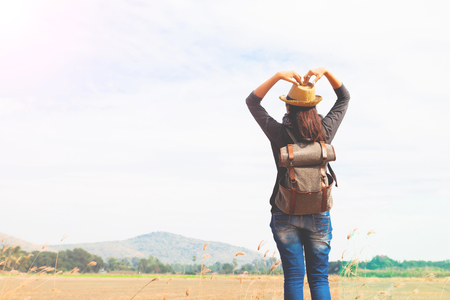 Happy woman traveler looking to blue sky and hands love sign, wanderlust travel concept, space for textの写真素材