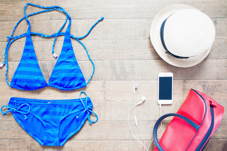 vacation, travel, tourism, technology and objects concept - close up of smartphone and beach stuff, flat lay on woodの写真素材