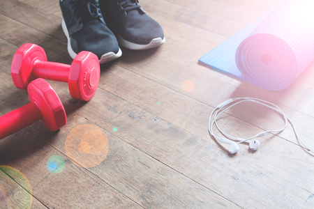 Fitness concept with sneakers, red dumbbells, yoga mat and earphones on wood floor, Copy spaceの写真素材