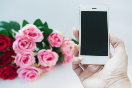 Woman hand holding mobile phone with rose bouquet backgroundの写真素材