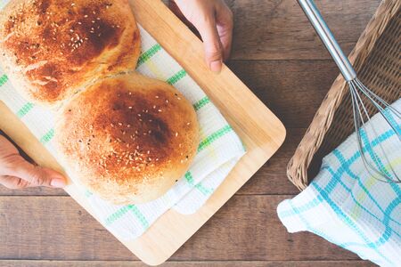 Woman hand holding loaf of bread on wooden plate