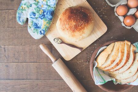 Loaf and sliced homemade bread with sesame, eggs and kitchen tools on wood backgroundの写真素材