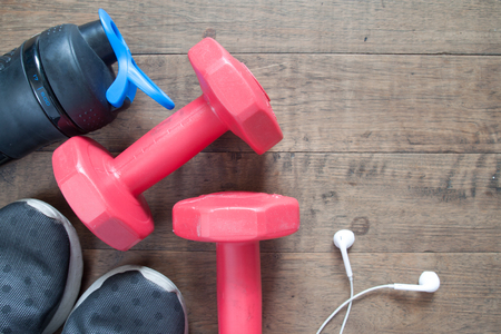 Flat lay of fitness and workout accessories, red dumbbells, water bottle and sneakers on wood backgroundの写真素材