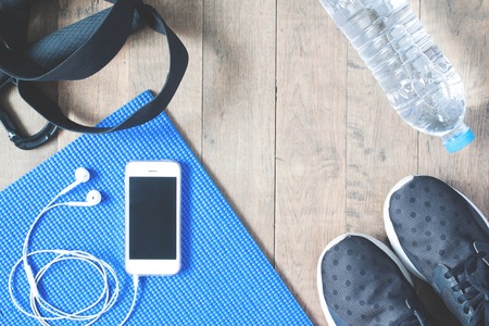 Flat lay of mobile phone with earphones and sport equipments on wood background. Workout and fitness items, top viewの写真素材