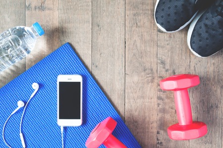 Flat lay of mobile phone with earphones and sport equipments on wood background. Workout and fitness items, top viewの写真素材