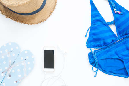Overhead view of blue color swimwear with smartphone, sandal and hat with copy space on white backgroundの写真素材