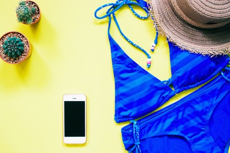 Blue color swimwear with smartphone, cactus and hat flat lay on yellow background, Summer vacation conceptの写真素材