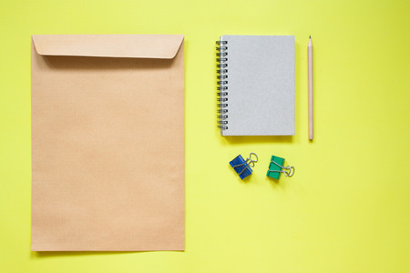 Brown envelope and notebook with stationery on yellow backgroundの写真素材