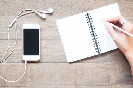 Overhead view of smartphone with empty notebook and woman holding pencilの写真素材