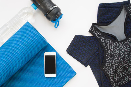 Overhead view of mobile device, yoga mat, yoga clothing and bottle of water on white background