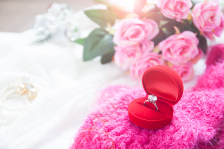 Wedding ring, Diamond ring in red box with pink roses and bride accessories. Selective focus