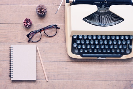 Creative flat lay of vintage workspace desk with typewriter, glasses and notebook, Wooden texture deskの写真素材