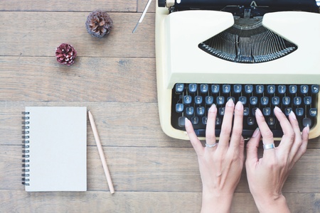 Creative flat lay of vintage workspace desk with woman hands on typewriter, Wooden texture deskの写真素材