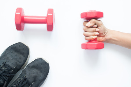Creative flat lay of woman hand holding red dumbbell with sport items on white backgroundの写真素材