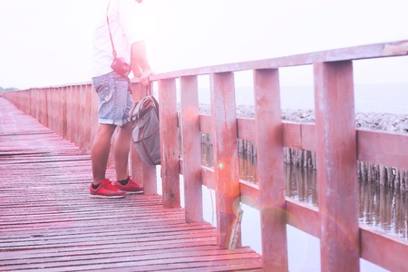 Asian man with camera and bag standing on wooden bridge seeing around beach and sand, Summer travel の写真素材