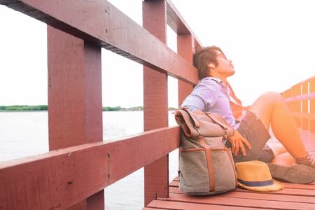 Summer vacation with sunshine, Asian backpacker relaxing on wooden bridgeの写真素材