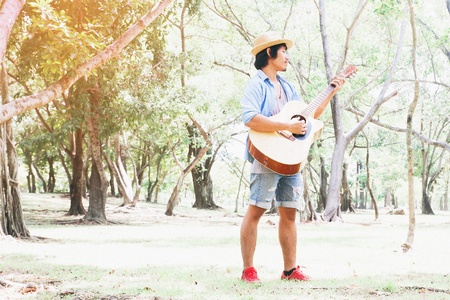 Happy man in casual jeans and straw hat playing guitar in parkの写真素材