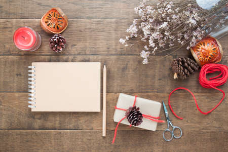 Creative flat lay of Christmas gift box, ornaments, winter accessories and craft notebook on wood background, Top viewの写真素材