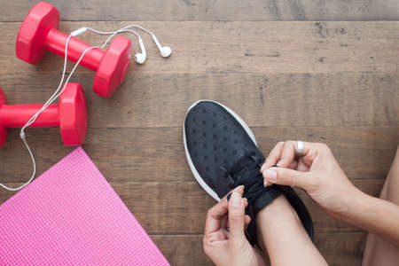 Overhead view of woman hands tying shoes with sport equipments on wood background