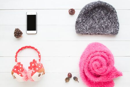 Creative flat lay mock up of smart phone and winter accessories for girl on white wooden background for beauty and travel applicationの写真素材