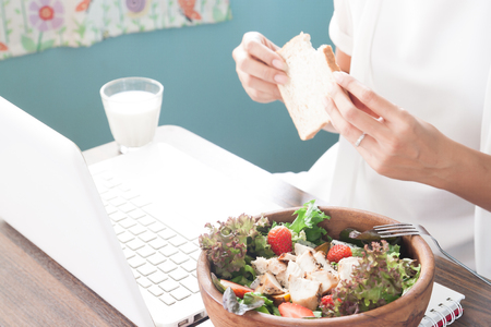 Working woman with morning meal, Selective focus on salad and woman holding sliced bread in backgroundの写真素材