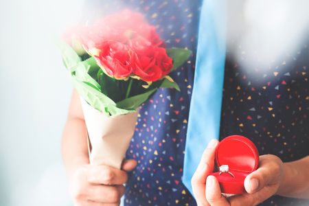 Close up man in casual shirt and necktie holding diamond ring and roses bouquetの写真素材