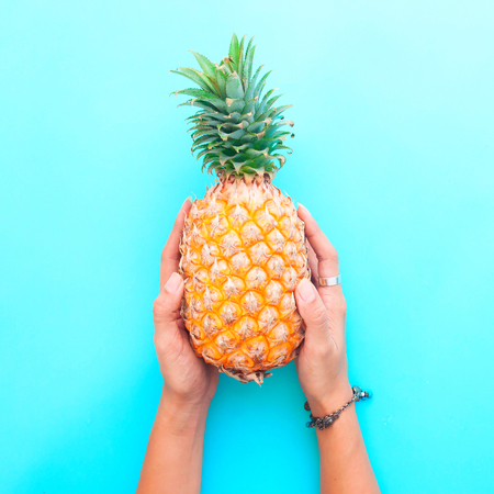 Woman's hands holding pineapple on blue color background, Summer holiday conceptの写真素材