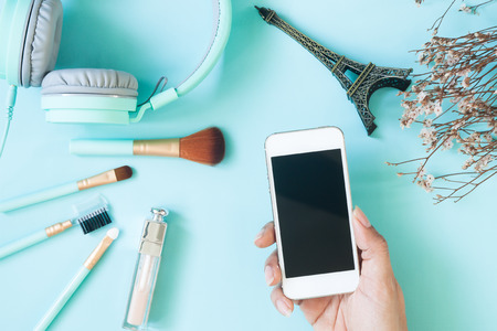 Beauty overhead view shot with woman hand holding smart phone with cosmetic and beauty items, Pastel...