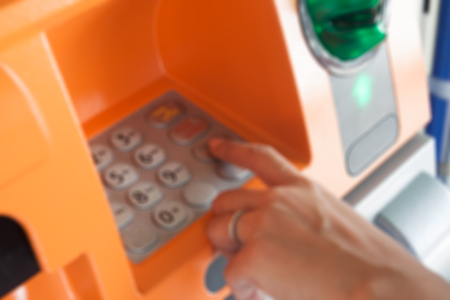 Blurry background of woman's hand enter code on ATM machine, Banking or financial concept backgroundの写真素材
