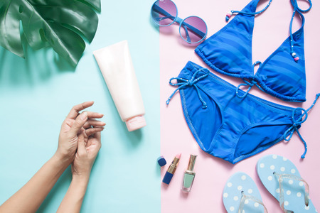 Beach accessories, Bikini, sunglasses, sandals with woman's hands and beauty products on pastel color background, Summer beauty conceptの写真素材