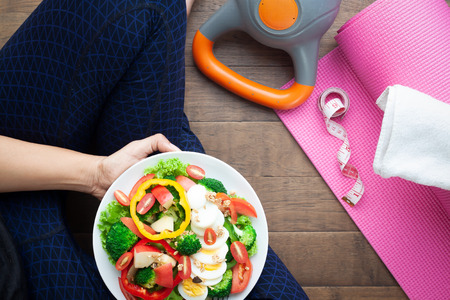 High angle view woman wearing yoga clothing eat salad, Fitness and yoga equipments on wooden floor. Beauty and Healthy conceptの写真素材