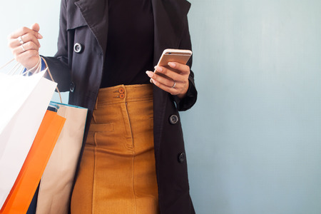 Woman wearing black overcoat using mobile phone and shopping bags on hand, Shopping conceptの写真素材