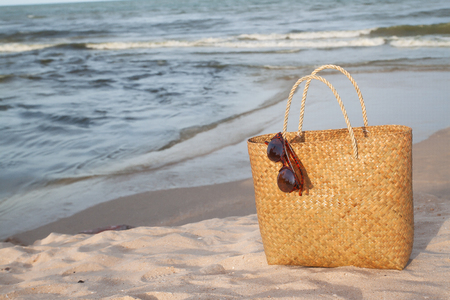 Straw bag with sunglasses on the beach and sunset lightの写真素材