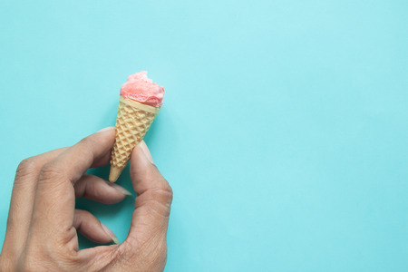 Woman's hand holding bitten pastel meringue on ice cream cone with blue backgroundの写真素材