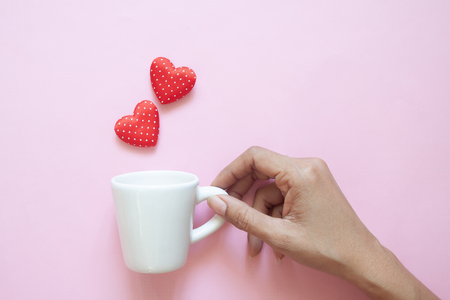Creative flat lay, woman hand holding white cup with polka dots red hearts on pink background.の写真素材
