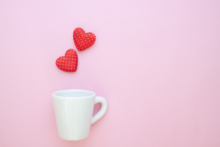 A white cup with polka dots red hearts on pink background. Copy spaceの写真素材